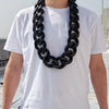 A man wearing a white t-shirt displays a chunky black acrylic Cuban link necklace.