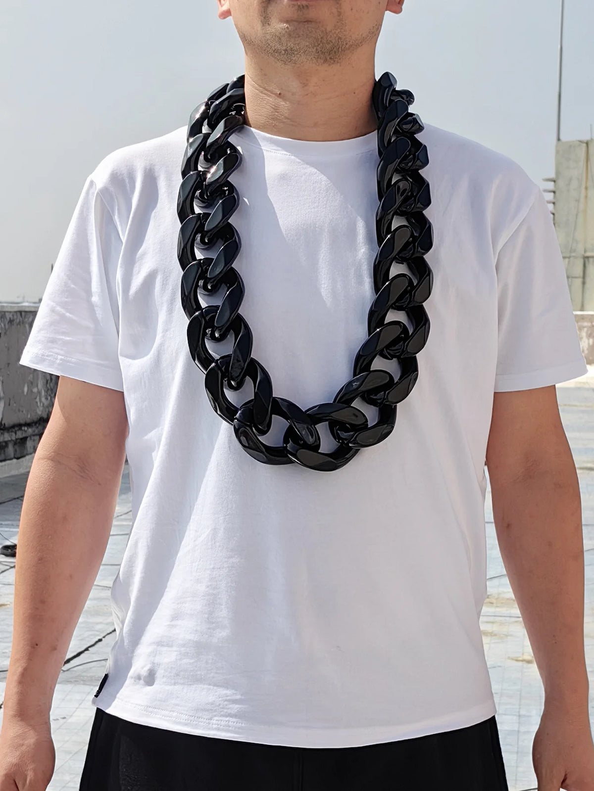 A man wearing a white t-shirt displays a chunky black acrylic Cuban link necklace.
