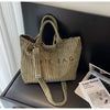 Sac à épaule en velours à rayures vert olive texturé, suspendu sur fond sombre.
