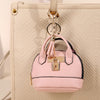 Portefeuille en plastique rose luxueux avec clé, suspendu à une sangle en cuir sur fond beige texturé.