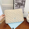Funda acolchada beige para portátil con patrón floral sobre un cuaderno azul claro.