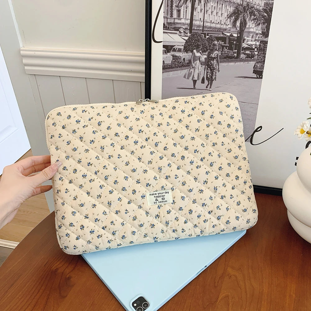 Funda acolchada beige para portátil con patrón floral sobre un cuaderno azul claro.