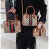 A woman holds an elegant leather tote diaper bag with a crossbody strap featuring green and red stripes.