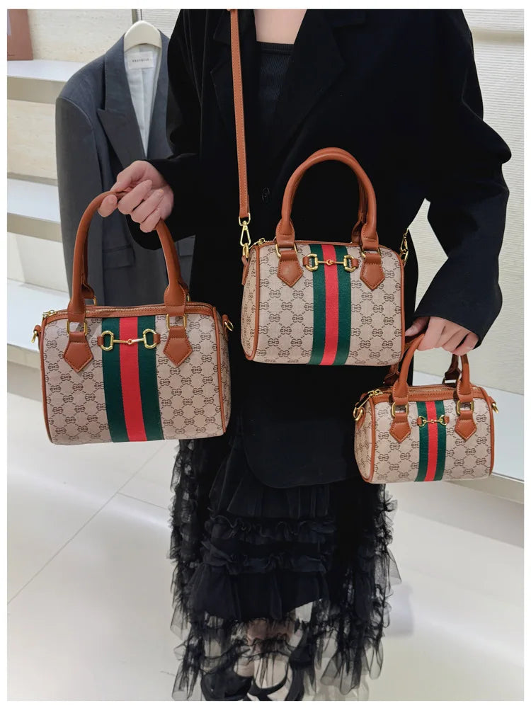 A woman holds an elegant leather tote diaper bag with a crossbody strap featuring green and red stripes.