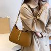 A woman wearing a beige trench coat holds a tan leather hobo shoulder bag.