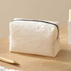A rectangular cream-colored lace mesh organizer bag resting on a wooden surface with a gold applicator visible.