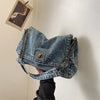 A blue denim tote bag with a silver chain strap is displayed against a white wall.