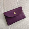 A deep purple genuine leather card holder with a gold-toned stud closure resting on a white textured surface.