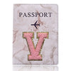 Cubierta de pasaporte de cuero marmolado rosa con una inicial V dorada y un ícono de avión.