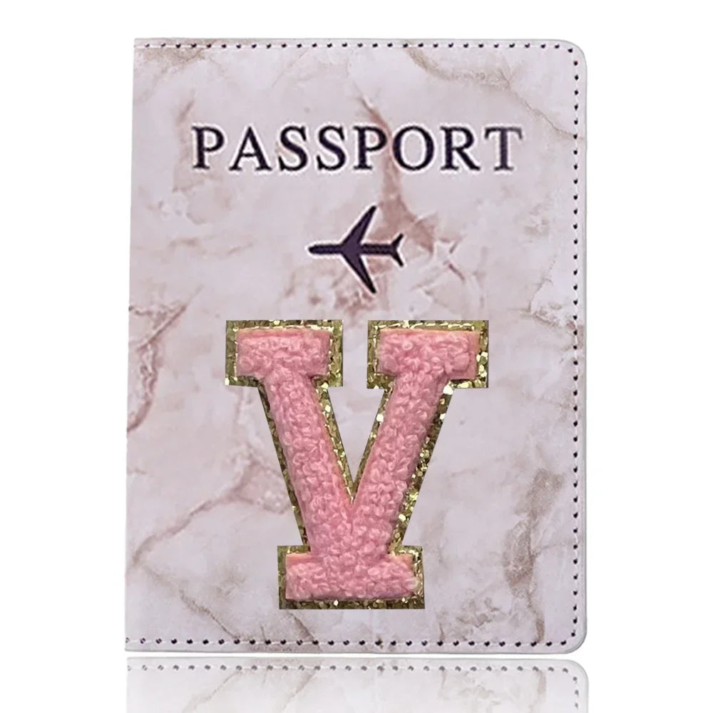 Cubierta de pasaporte de cuero marmolado rosa con una inicial V dorada y un ícono de avión.