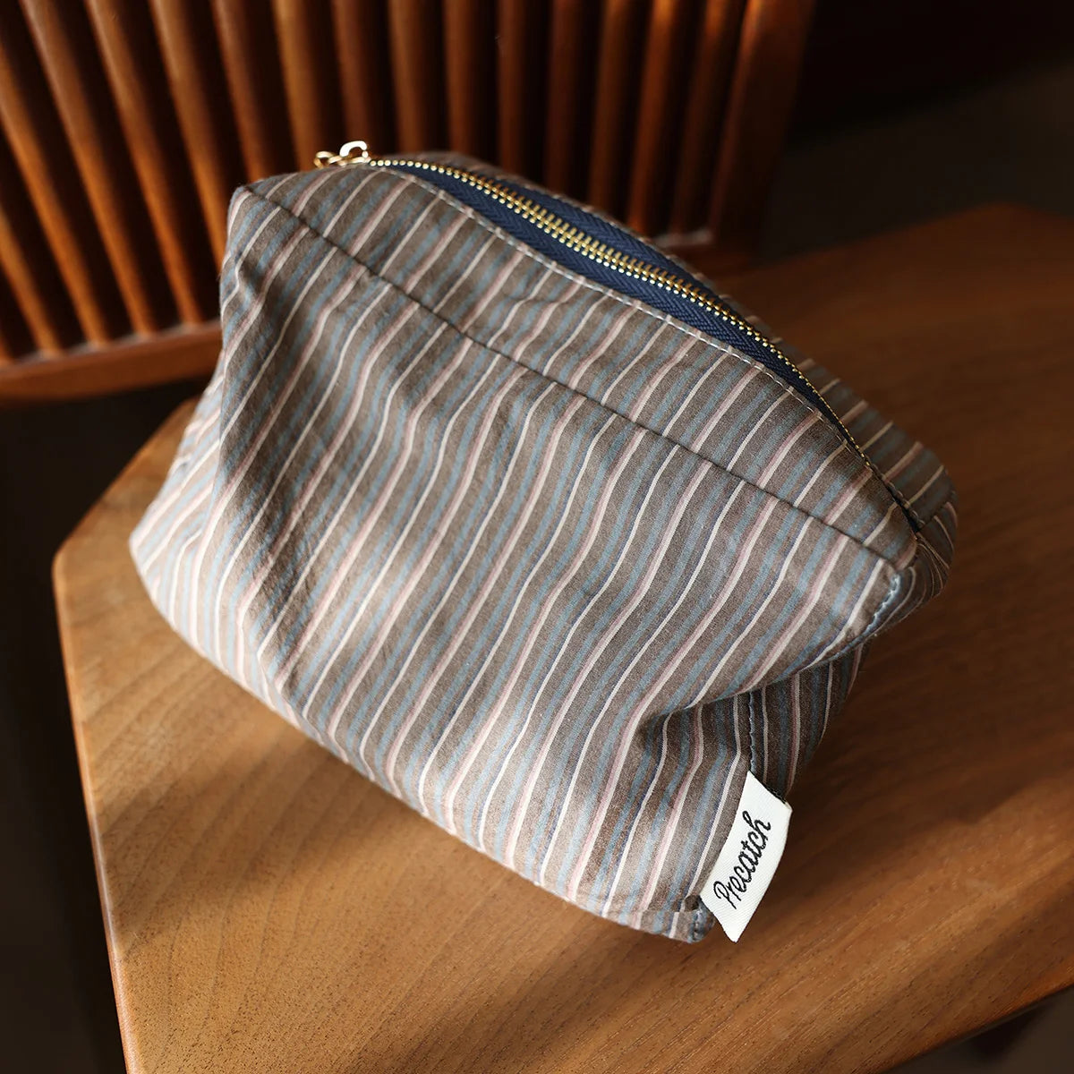 Pochette de rangement cosmétique à rayures gris et beige avec fermeture éclair marine sur une surface en bois.