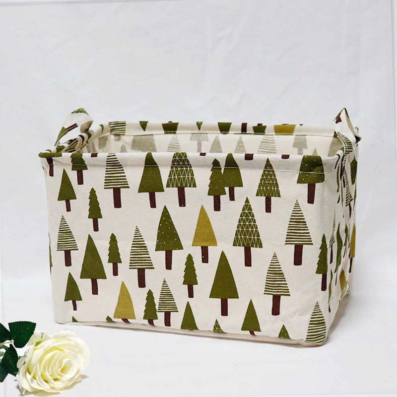 A beige fabric storage basket with handles featuring a repeating pattern of green and brown pine trees.