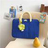 A blue quilted laptop sleeve with a light yellow handle and charm resting on a white surface.