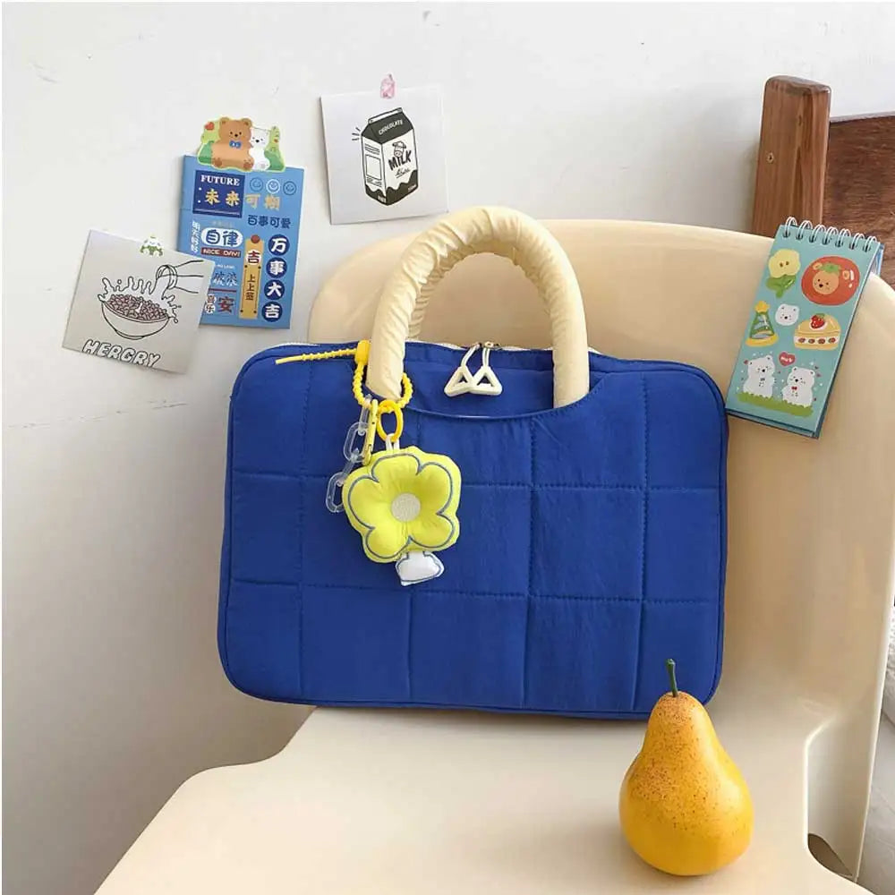 A blue quilted laptop sleeve with a light yellow handle and charm resting on a white surface.
