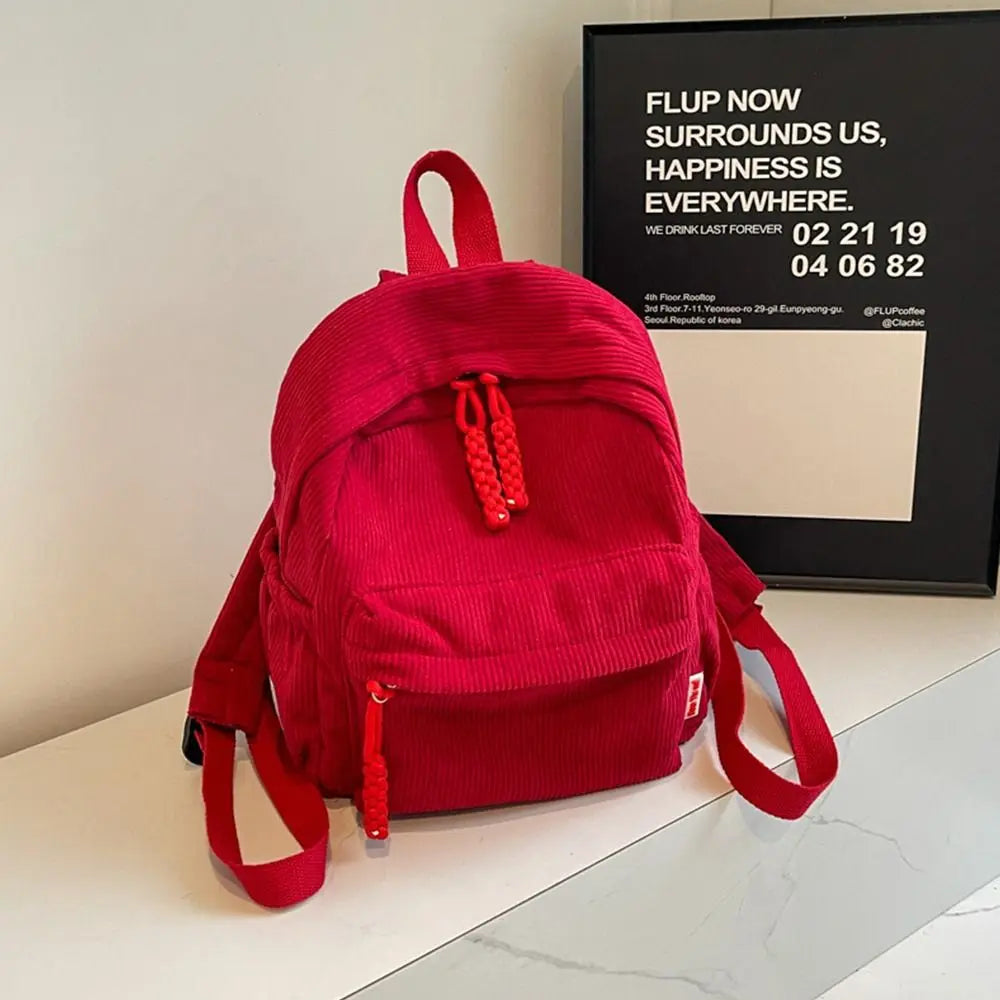 A bright red lightweight corduroy daily backpack is displayed on a white surface.