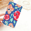 A hand holds a colorful floral design card holder with pink and red flowers on a blue background.
