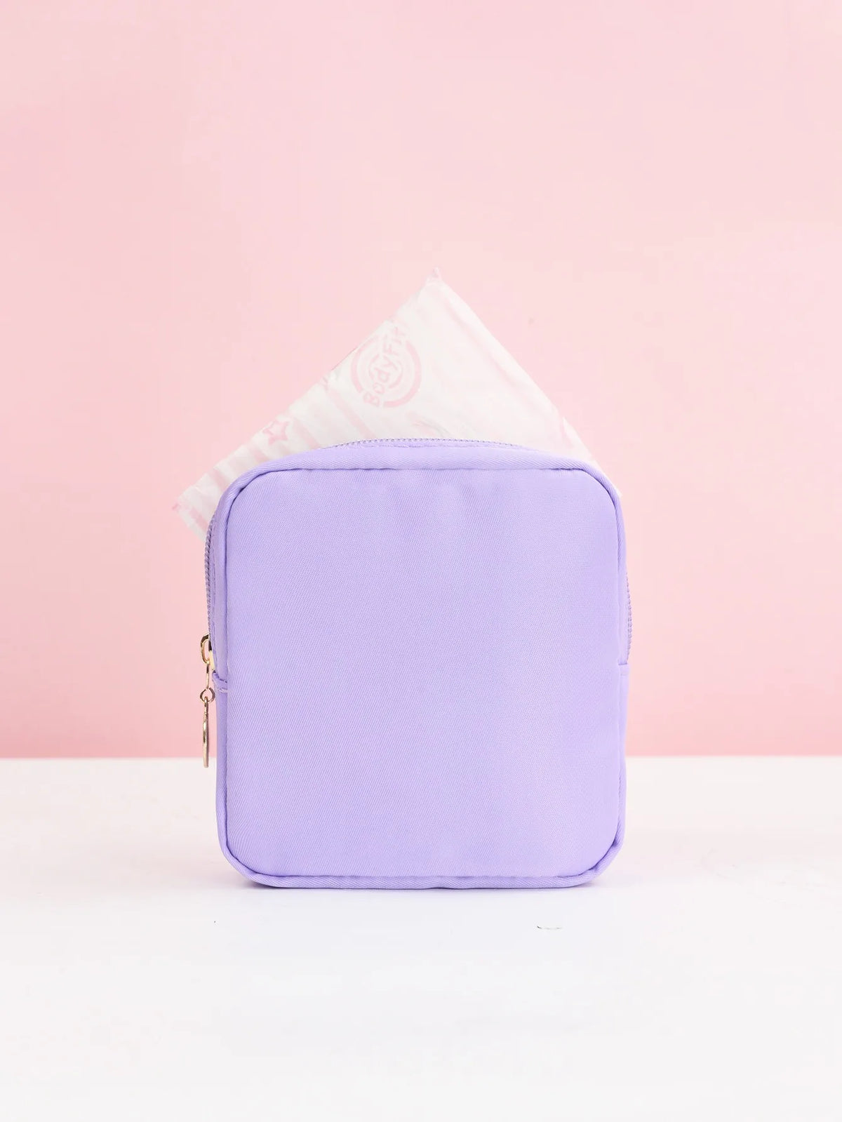 Lila Aufbewahrungstasche für Damenbinden mit weißem Papiertupfer, vor rosa Hintergrund.