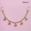 Gold chain necklace with pink bead pendants displayed on a light pink background.
