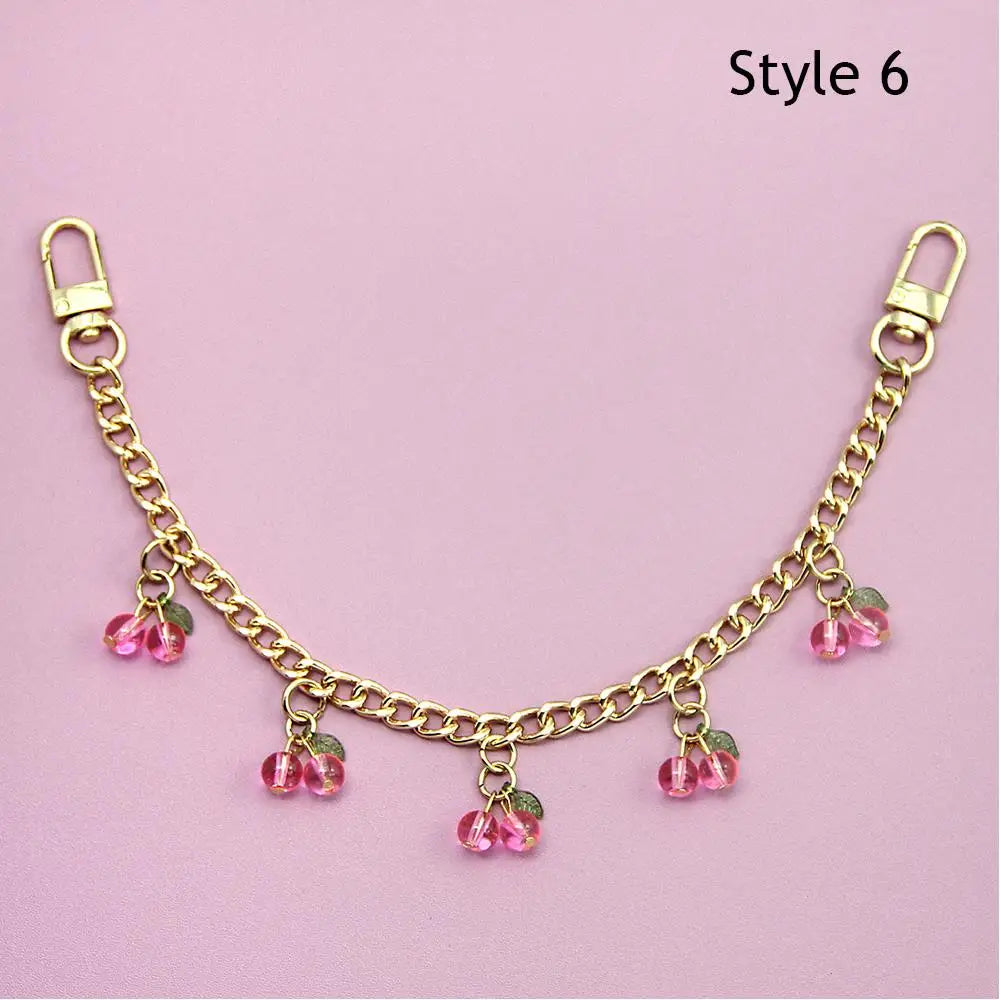 Gold chain necklace with pink bead pendants displayed on a light pink background.