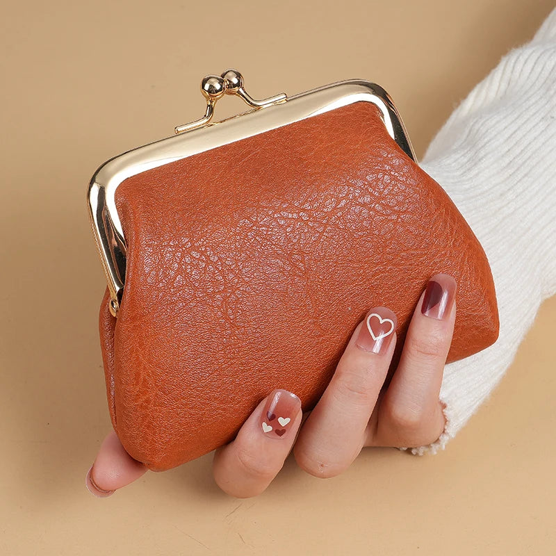 A brown leather coin purse with a gold buckle is held by a hand next to a white knitted sleeve.
