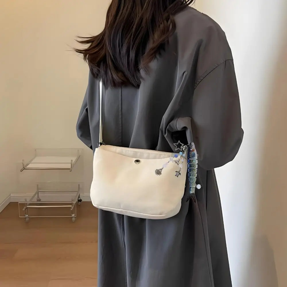 A woman holds a cream-colored pouch with a blue and white simulation fish keychain against a gray garment.