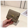 A hand holds a beige multi-slot card holder with a gold clasp on a light surface.