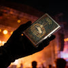 A hand holds an Art Deco metal card holder featuring an engraved design against a dark background.