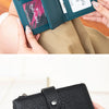 A hand holds a dark teal clutch wallet and a black leather clutch wallet.