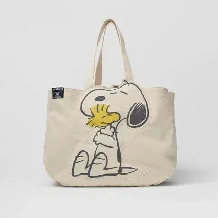 A beige canvas shoulder bag featuring a Snoopy cartoon design.