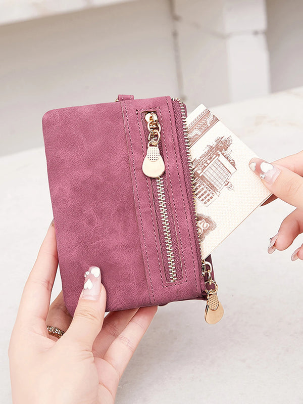 A hand holds a mauve retro PU leather double fold wallet with a gold zipper pull.