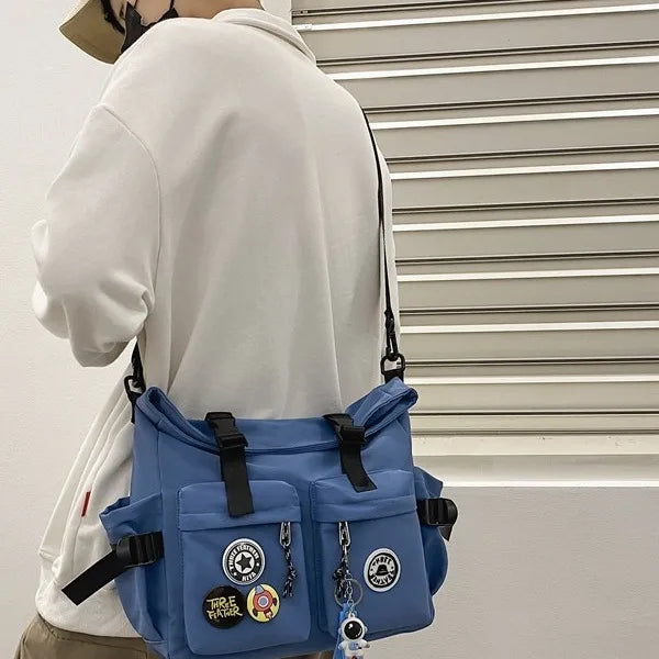 A light blue nylon crossbody bag with black accents is shown from the back, hanging against a white window blind.