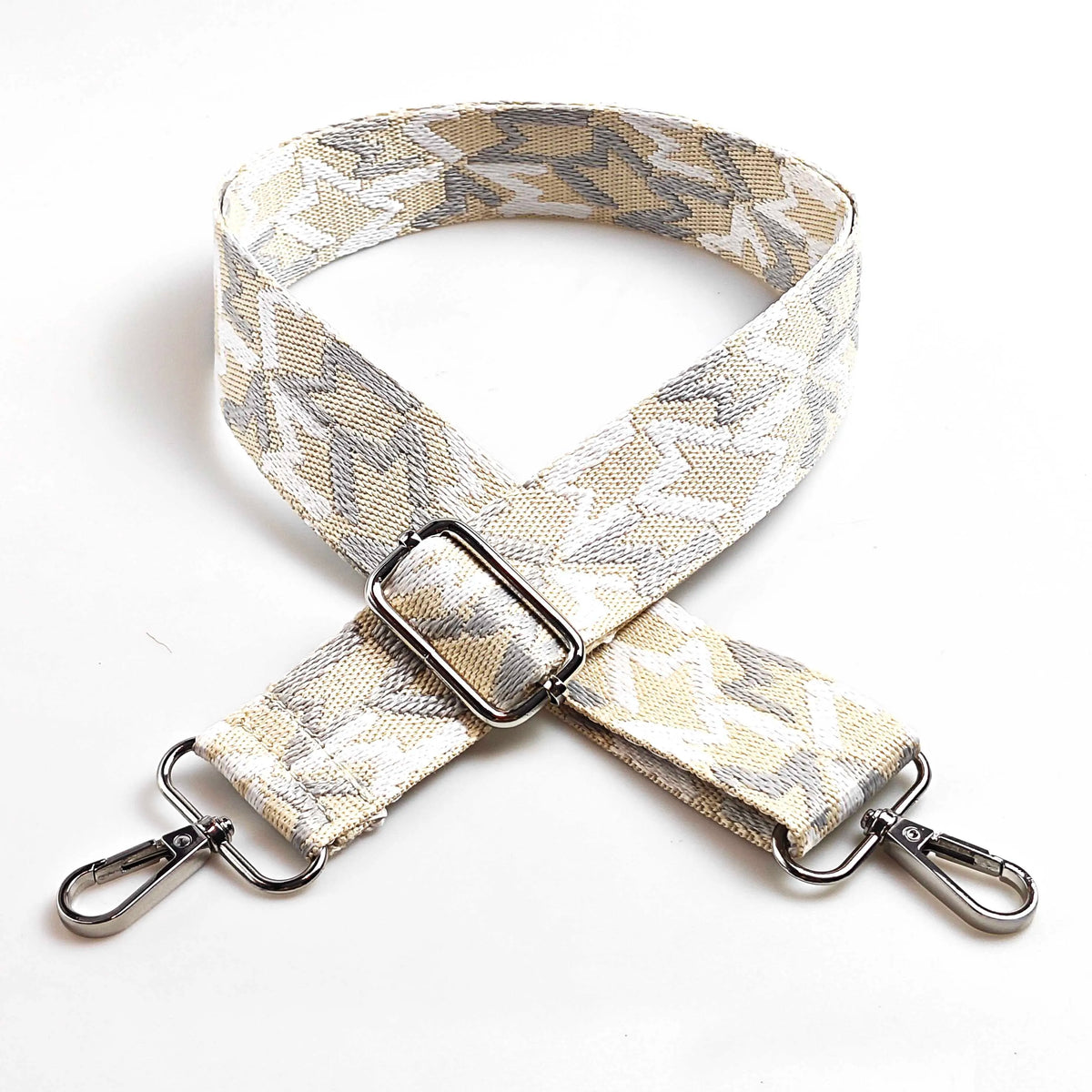 A beige and gray jacquard patterned adjustable crossbody bag strap with metal hardware.