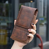 A brown PU leather phone waist pouch with a belt clip is held by a hand.