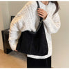 A woman wearing a cream knit sweater and black skirt holds a black suede slouchy shoulder bag.