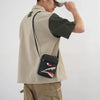Une personne portant un haut beige et un pantalon camel tient une pochette de téléphone noire avec motif crocodile.