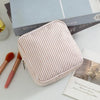 A light pink seersucker striped multi-functional storage pouch resting on a white surface next to makeup brushes and books.