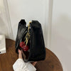 A black PU leather shoulder bag with a gold chain and cherry pendant is held by a hand.