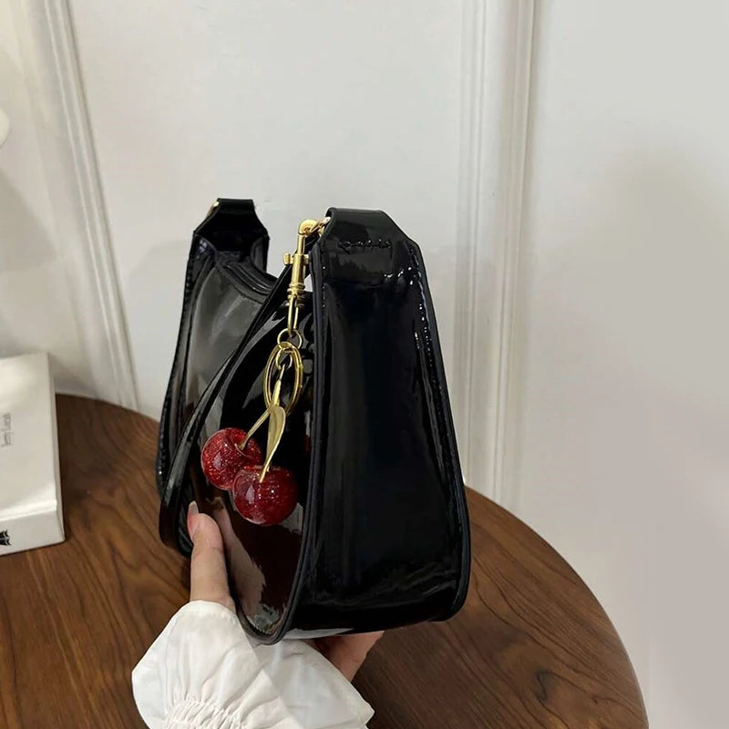 A black PU leather shoulder bag with a gold chain and cherry pendant is held by a hand.