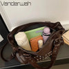 A brown punk rivet leather tote bag is shown open, revealing a pink cosmetic pouch and a purple spherical item inside.
