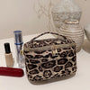 A dark brown leopard print faux suede cosmetic bag with a silver zipper sits on a white surface next to skincare products and