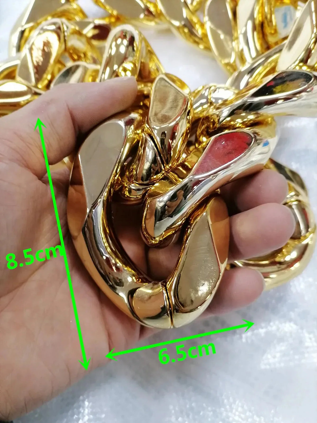 A hand holds a chunky gold acrylic Cuban link necklace, showing its size with a ruler.