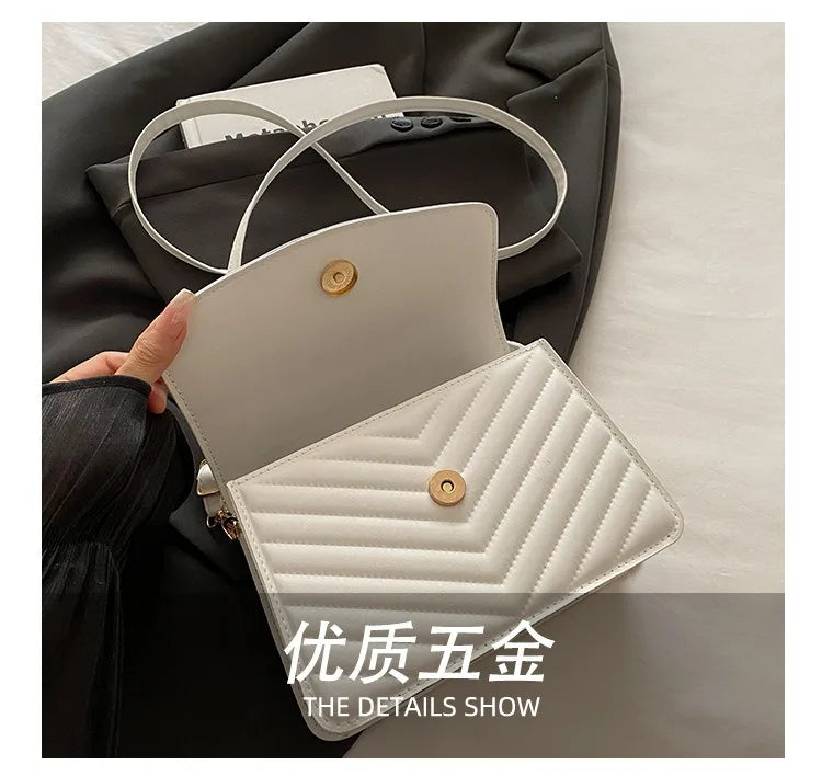 A close-up view of a white quilted shoulder bag with gold hardware, shown being held against a dark jacket.
