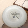 A silver pearl keychain with a heart pendant tied in a bow knot rests on a white ceramic plate.
