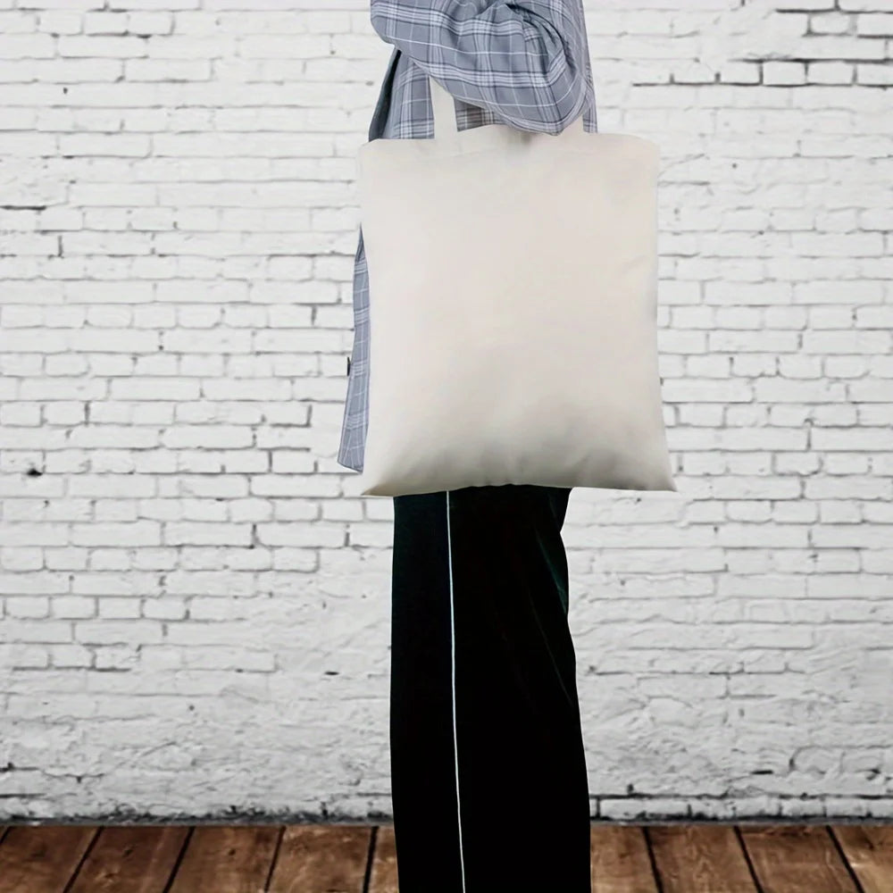 Un sac fourre-tout en coton blanc est exposé accroché à un vêtement contre un mur de briques blanches.