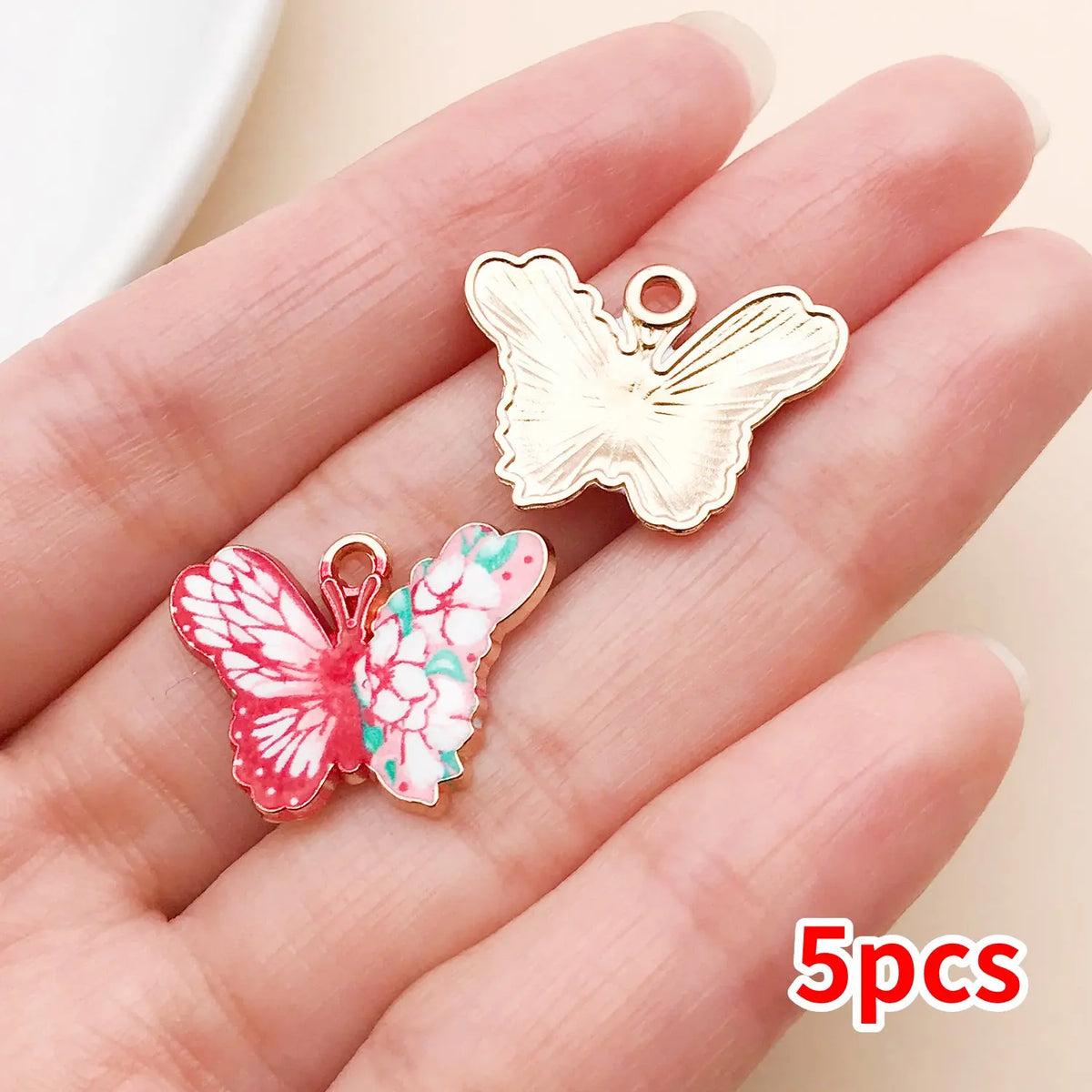 A set of five colorful butterfly enamel charms displayed on a hand.
