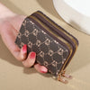 A hand holds a dark brown patterned zippered card holder wallet with gold zipper details.