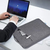 A person places a gray laptop sleeve containing a silver item on a white desk next to an open laptop.