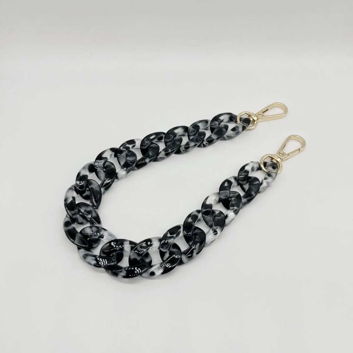 A close-up of a black and white marbled acrylic chain bracelet with gold-toned clasps.
