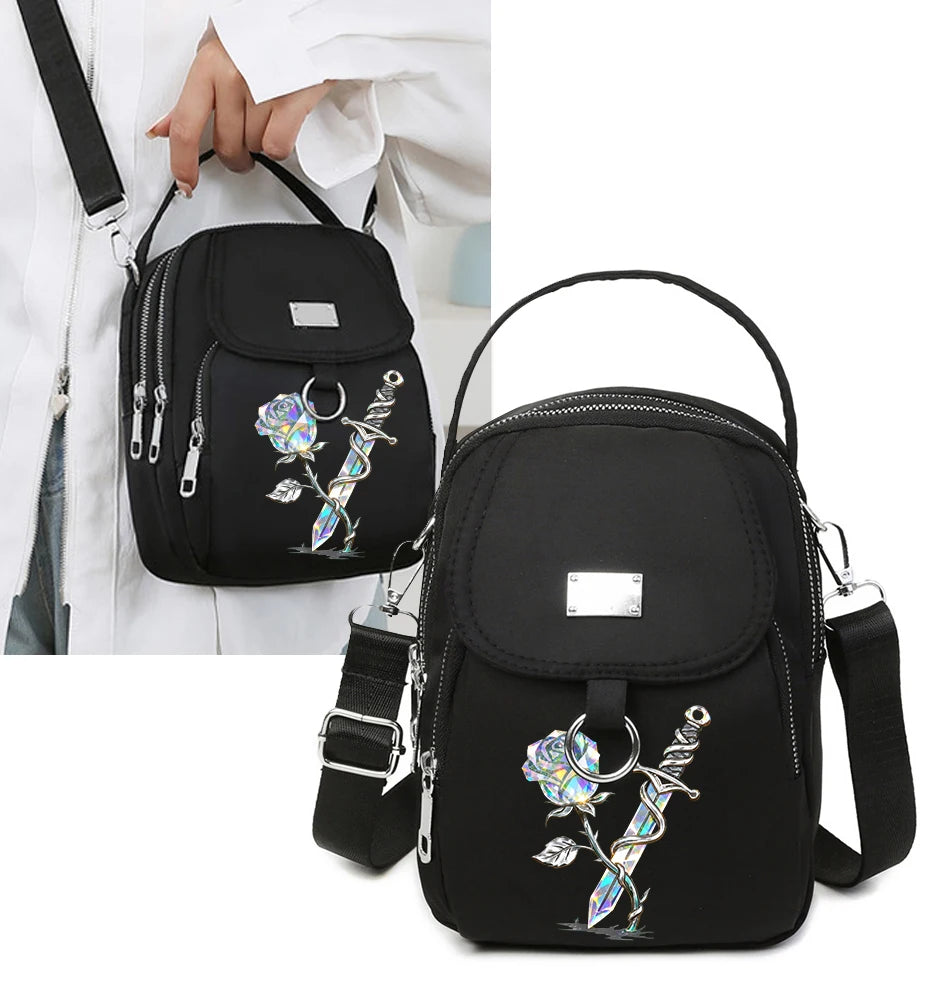 Sac bandoulière floral noir avec quincaillerie argentée tenu par une main