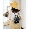 A woman wearing a beige top and yellow hat holds a black waterproof PU mini backpack.